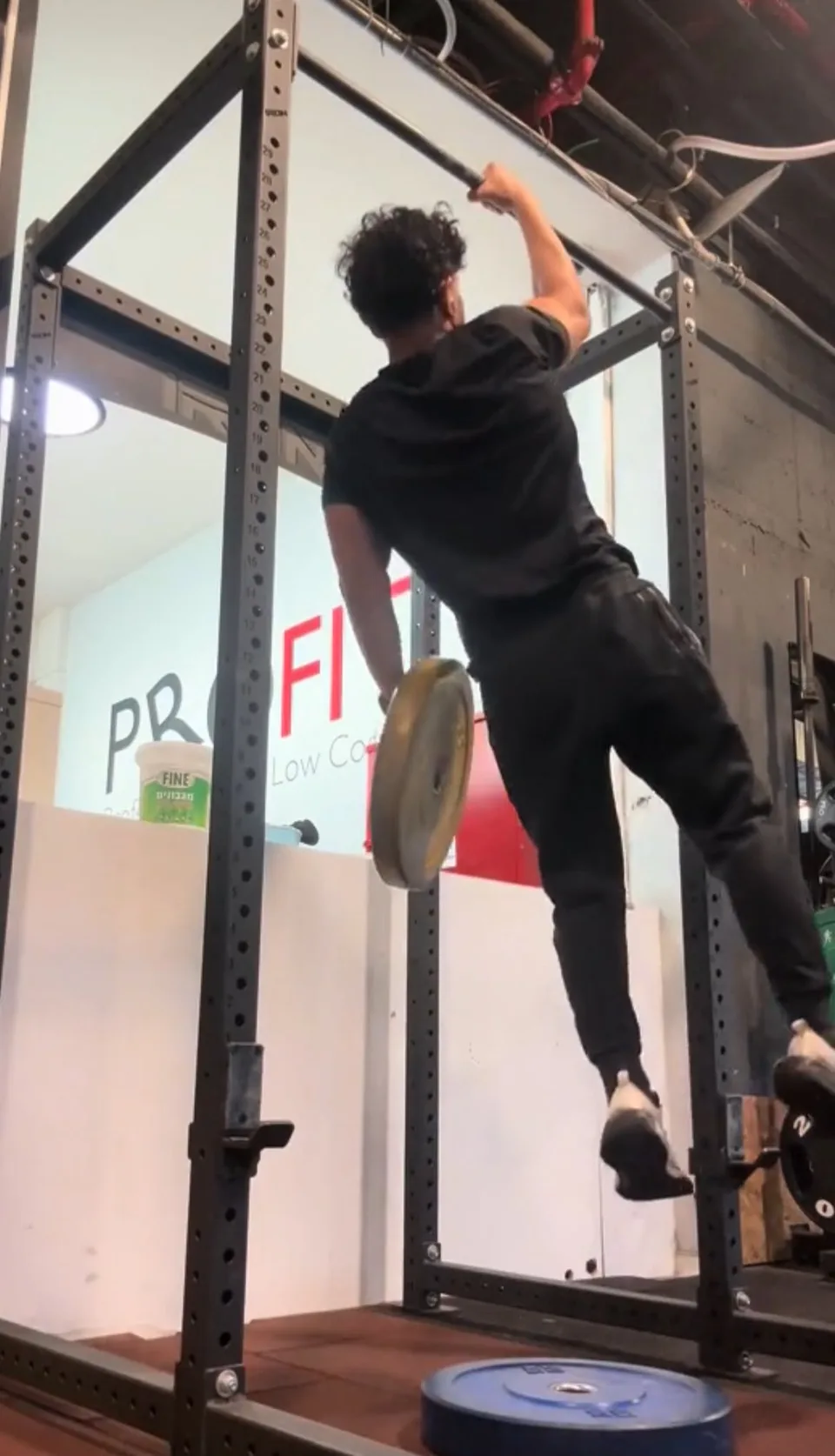 Ofek Zehavi gripping an overhead gym bar with one hand and holding a weight plate in the other