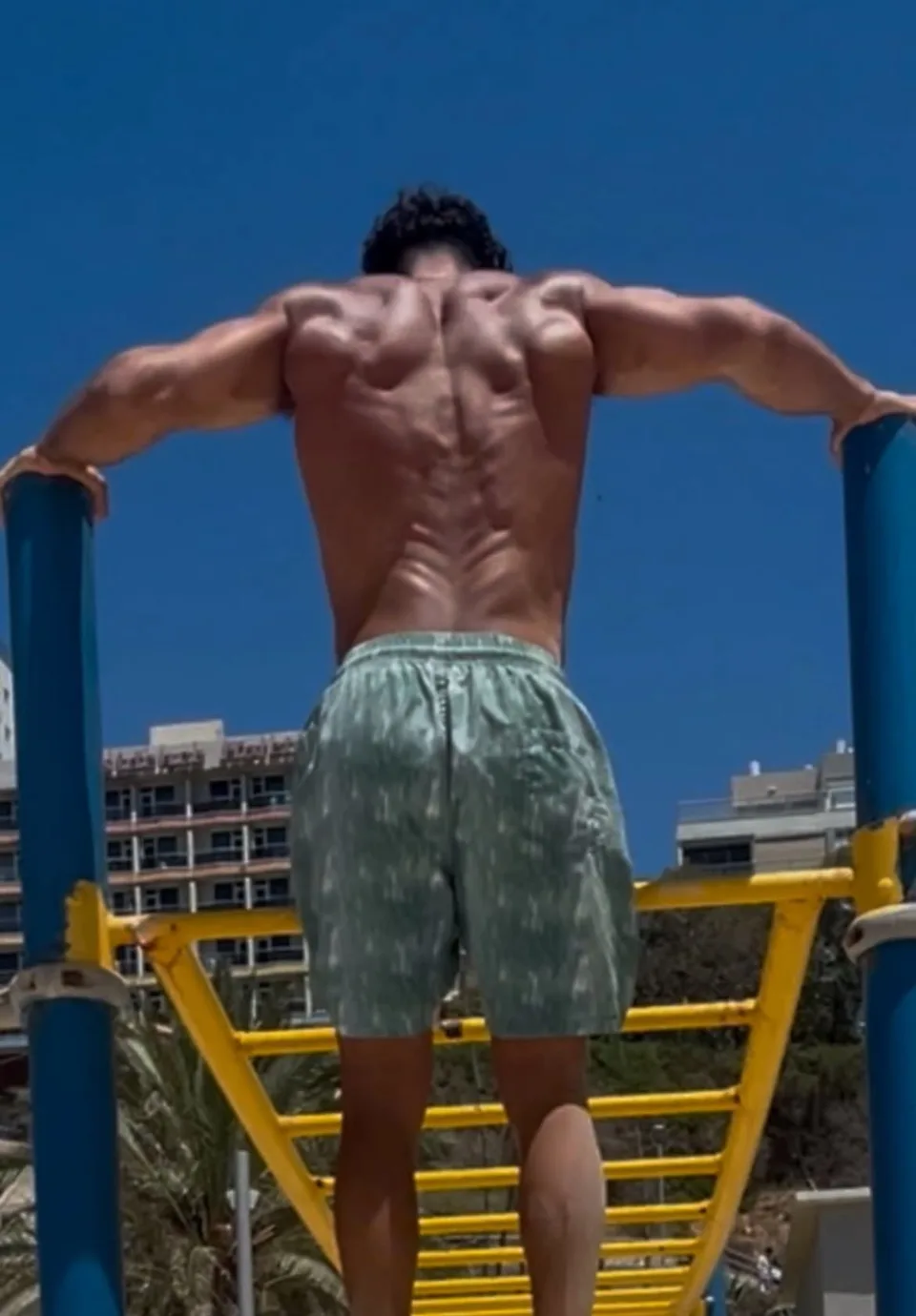 Ofek Zehavi seen from behind, supporting himself on outdoor exercise bars
